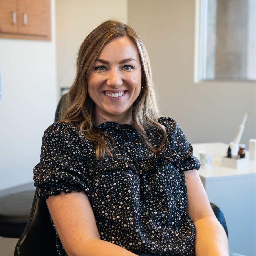 A woman is sitting in a chair in a dentist's office smiling at the camera.